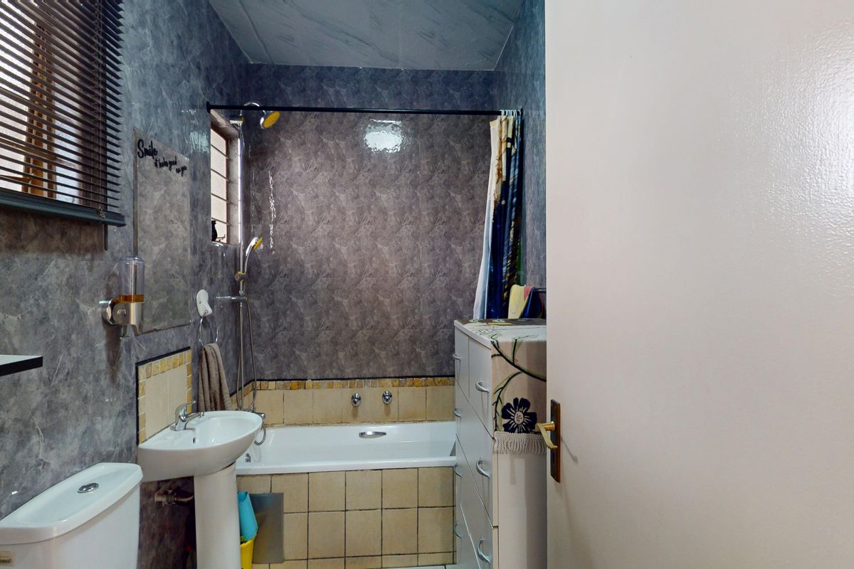 A functional bathroom featuring a pedestal basin, toilet, and a combined bathtub and shower area with tiled finishes.