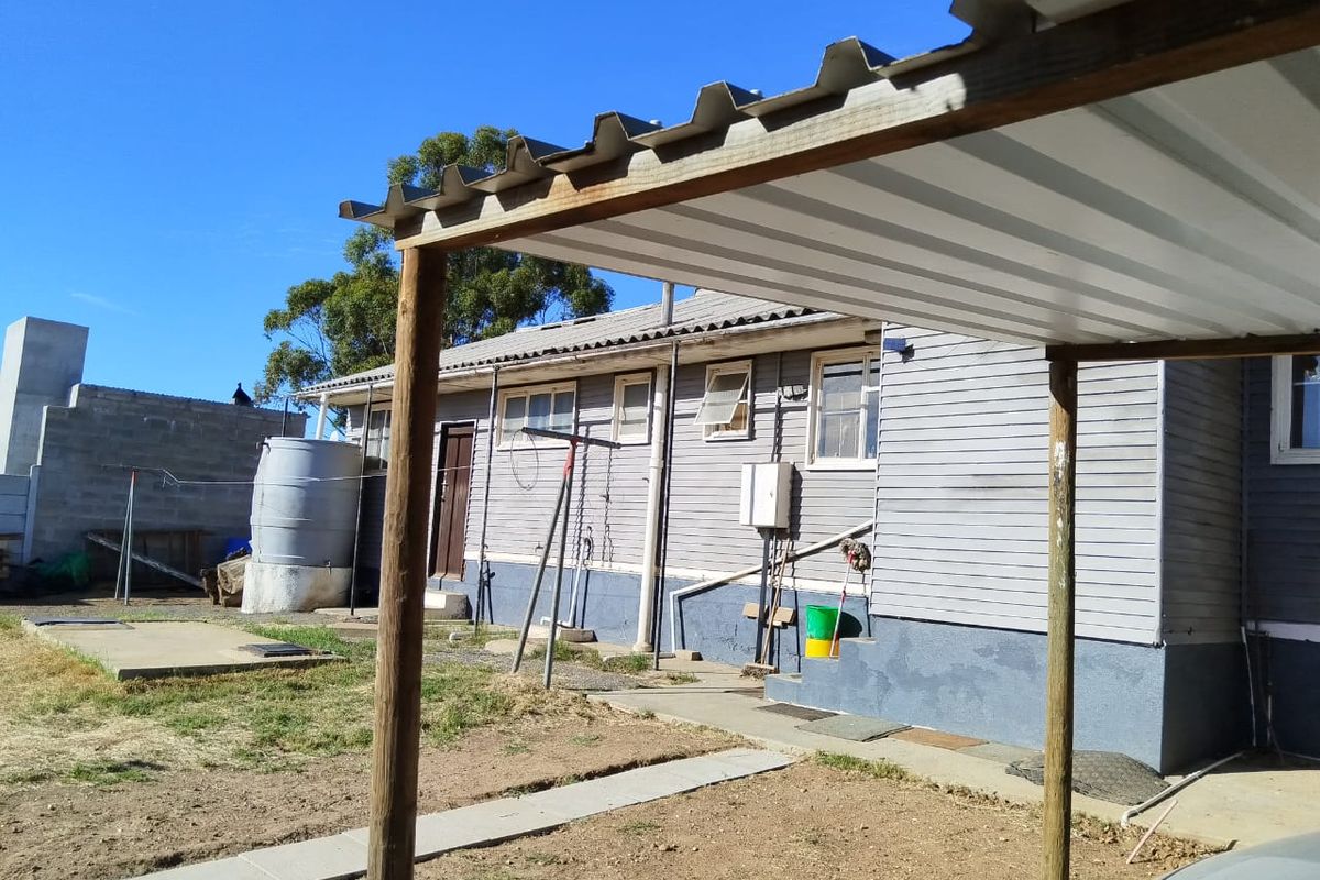 Rear view of the property featuring a corrugated metal carport structure, timber support posts, and exterior wall cladding with visible signs of wear.