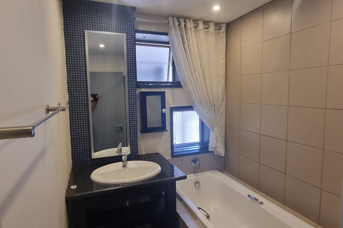 A functional bathroom featuring a vanity with a basin, a bathtub, and tiled wall finishes with a mosaic accent wall.