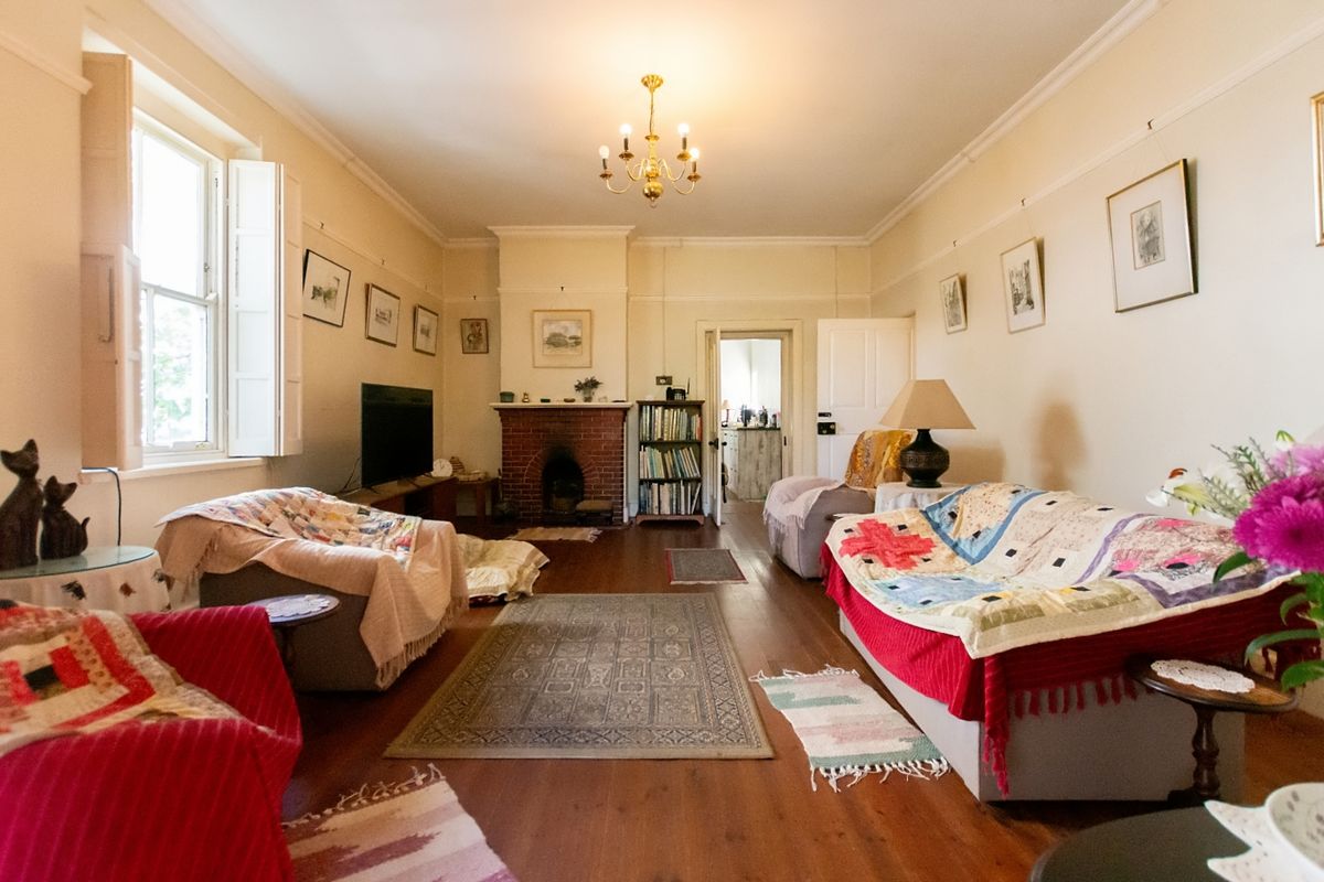 A spacious living room featuring original timber flooring, a classic brick fireplace, and traditional sash windows with internal shutters.