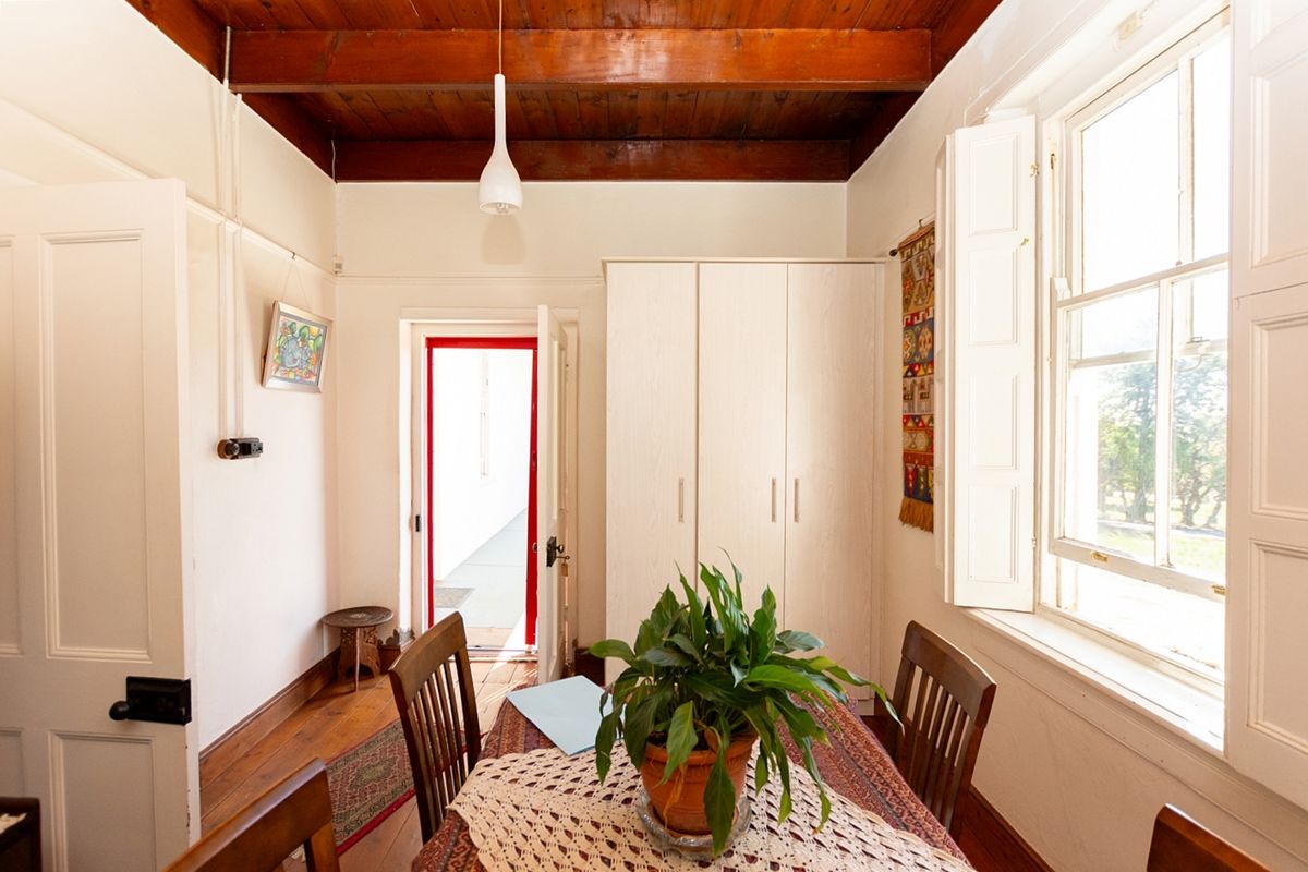 A bedroom featuring exposed timber ceiling beams, hardwood flooring, built-in wardrobe cabinetry, and traditional window shutters.