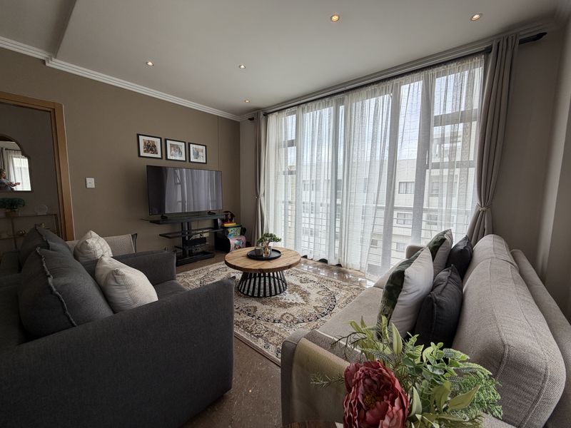 A well-maintained living room featuring recessed downlights, decorative ceiling molding, and large windows that provide ample natural light.