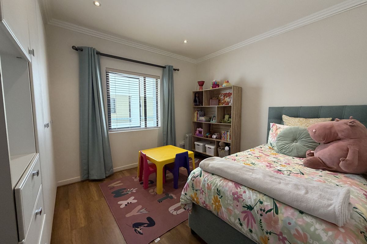 A well-maintained bedroom featuring laminate flooring, built-in cupboards, recessed downlighting, and decorative cornicing, offering a clean and functional living space.