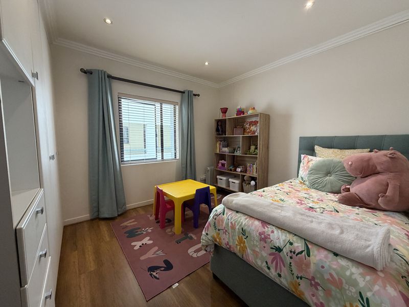 A well-maintained bedroom featuring laminate flooring, built-in cupboards, recessed downlighting, and decorative cornicing, offering a clean and functional living space.