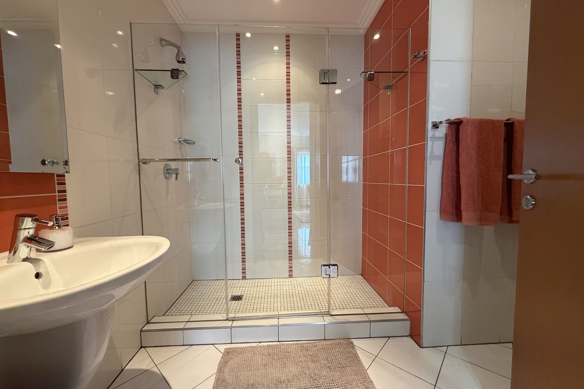 Modern bathroom featuring a spacious walk-in shower with glass enclosure, pedestal basin, and vibrant orange accent tiling.
