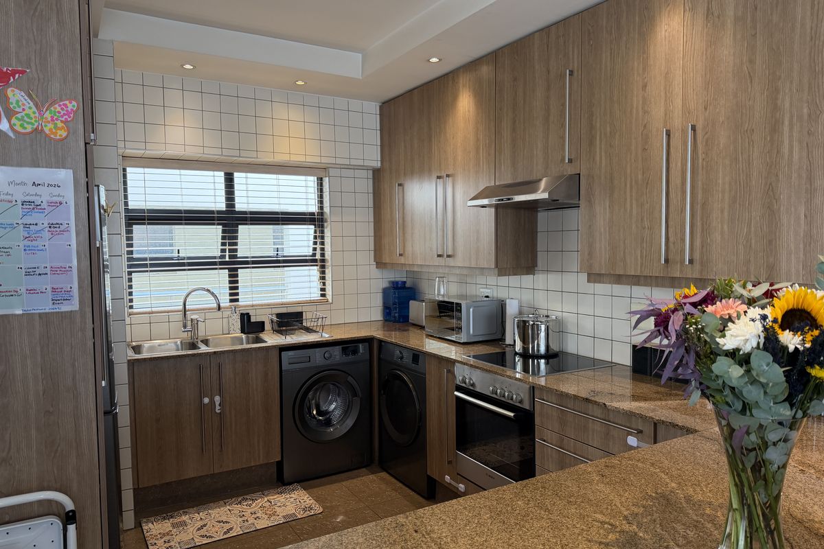 Modern kitchen featuring wood-finish cabinetry, granite countertops, integrated appliances, and a tiled backsplash with ample natural light.