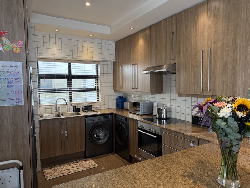 Modern kitchen featuring wood-finish cabinetry, granite countertops, integrated appliances, and a tiled backsplash with ample natural light.