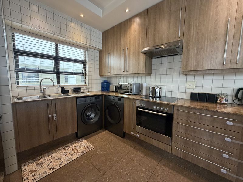 A well-maintained kitchen featuring wood-look cabinetry, granite countertops, integrated appliances, and a tiled backsplash with ample natural light from the window.