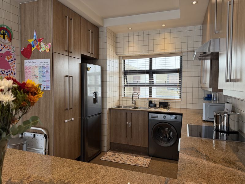 Modern kitchen featuring wood-look cabinetry, granite countertops, tiled backsplash, and integrated appliances including an electric hob and extractor fan.