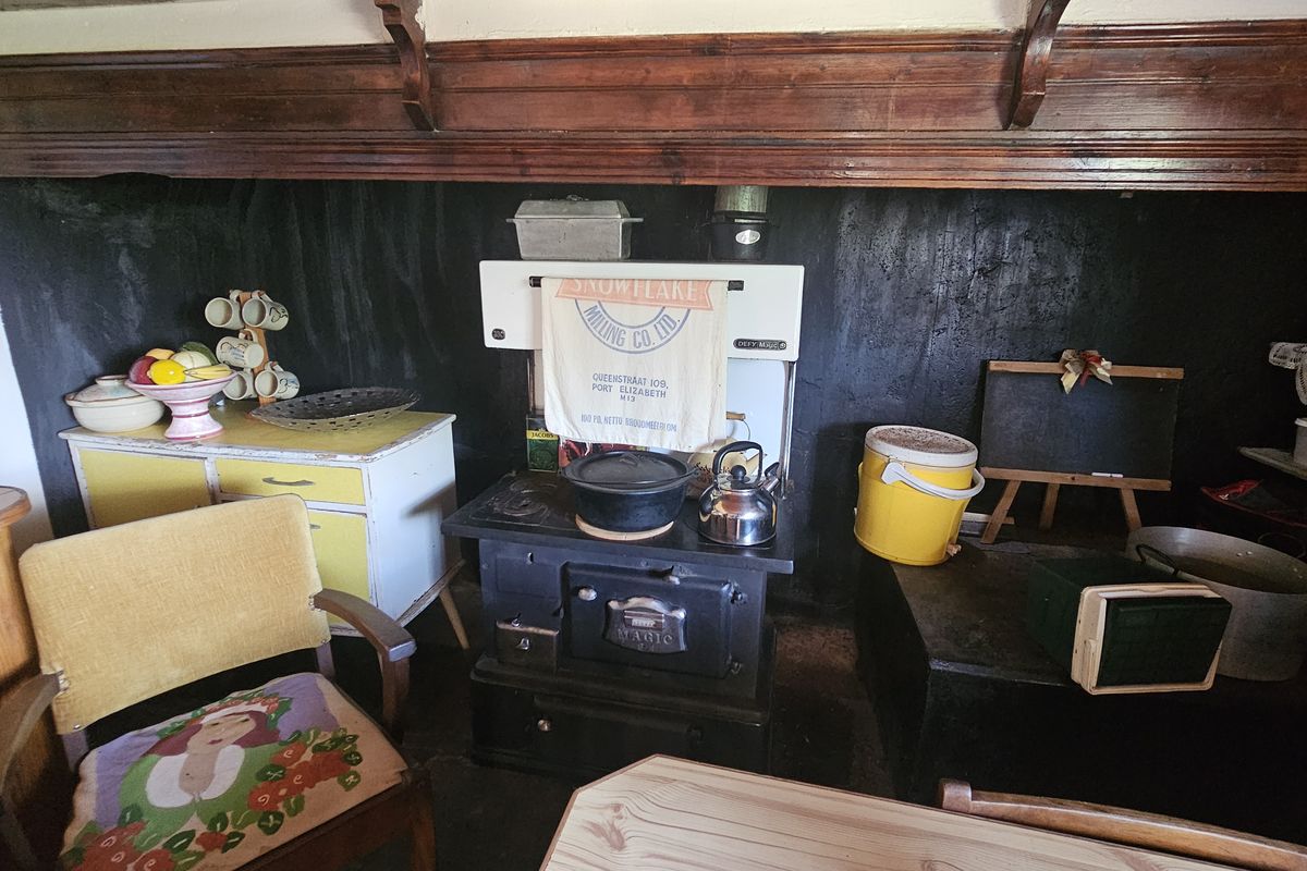 A rustic kitchen area featuring a vintage cast-iron stove set against a dark, textured wall with traditional wooden beam detailing.