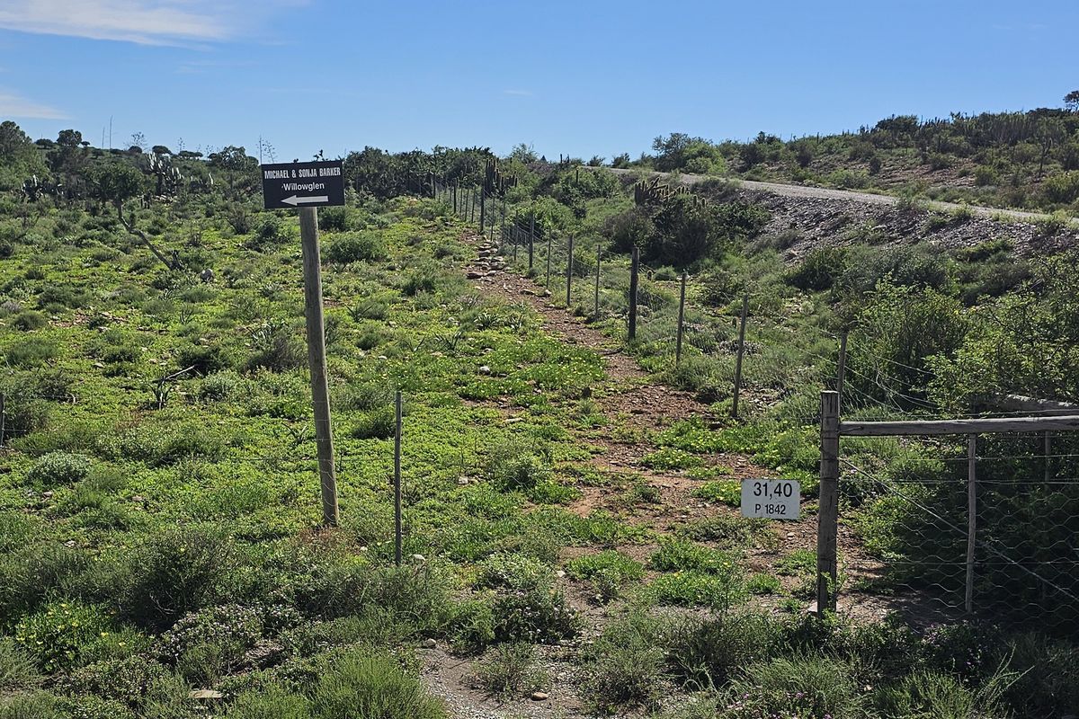 A view of the farm landscape featuring a wire fence boundary, gravel path, and signage indicating property access.