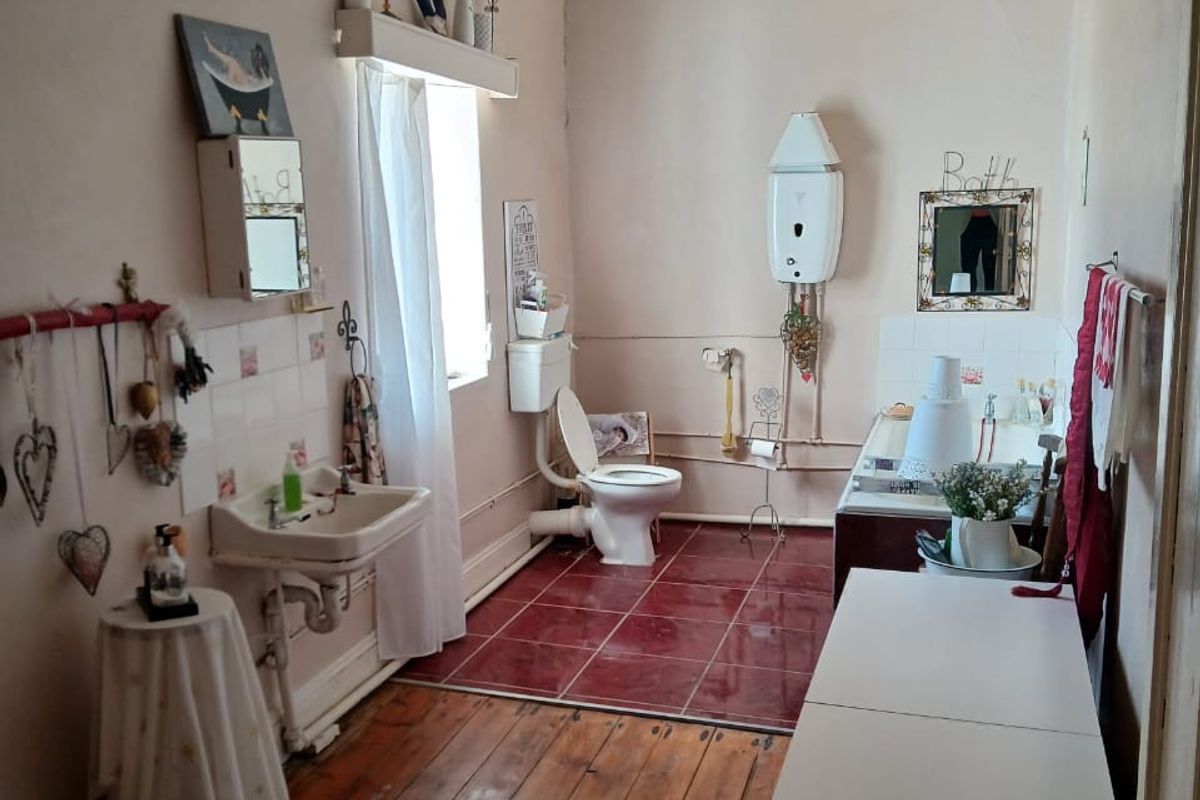 A dated bathroom featuring a wall-mounted gas geyser, tiled flooring, and original timber floorboards, offering potential for renovation and modernization.