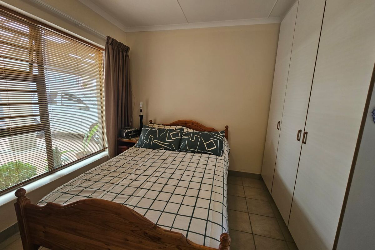 A functional bedroom featuring built-in cupboards, tiled flooring, and a large window with venetian blinds, offering a neutral space ready for personalization.