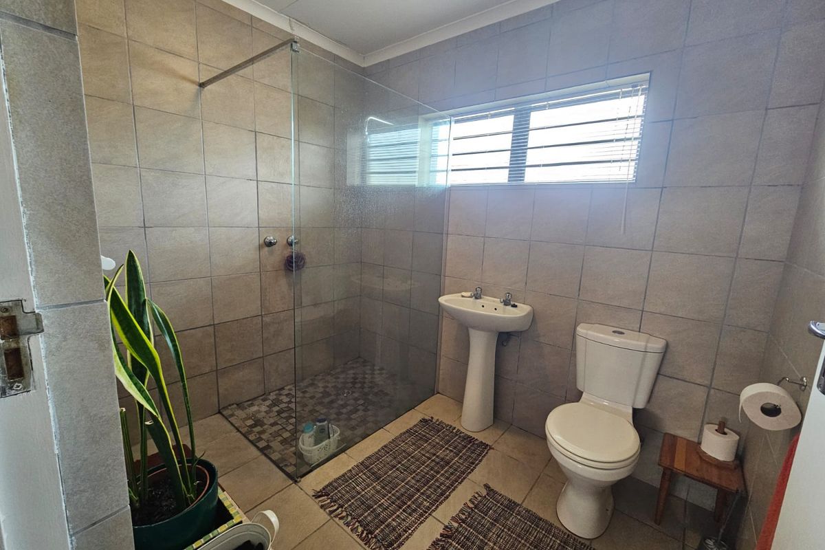 A functional bathroom featuring a walk-in shower with a glass screen, pedestal basin, and toilet, finished with neutral wall and floor tiling.
