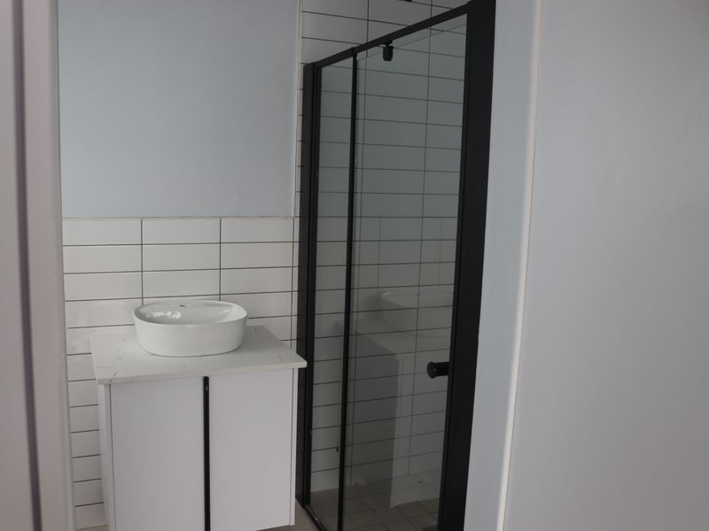 Modern bathroom featuring a vessel sink on a stone-topped vanity and a sleek shower enclosure with black framing and white subway wall tiles.