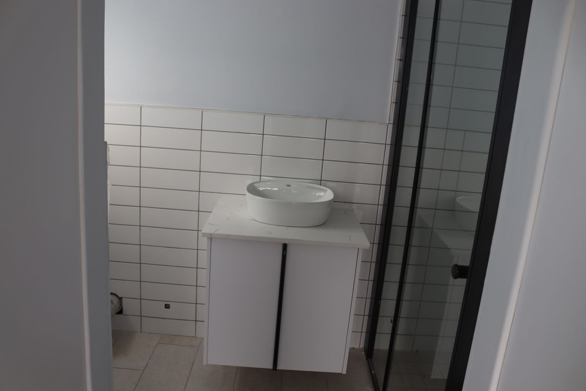 A modern bathroom featuring a white vanity with a vessel sink, subway tile backsplash, and a shower enclosure with a black frame.