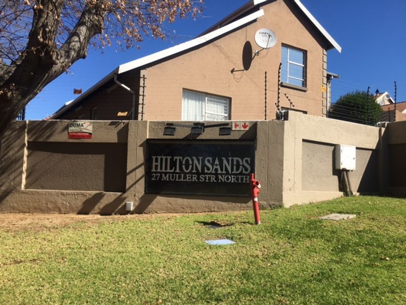 Street-facing view of the Hilton Sands complex entrance, featuring a perimeter wall with electric fencing and signage.