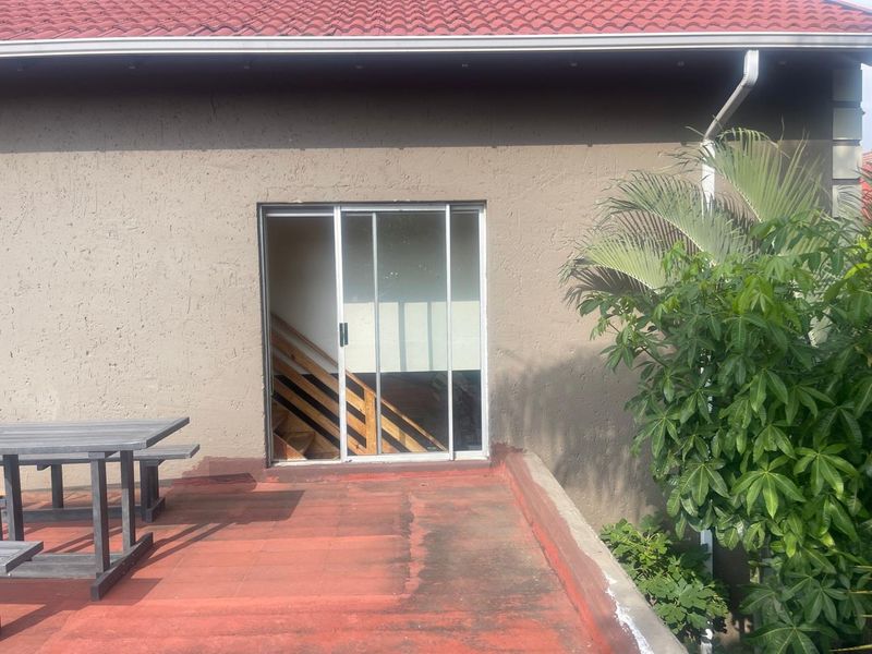 A rear patio area featuring a sliding glass door entrance, tiled flooring, and a roof overhang, providing direct access to the interior living space.