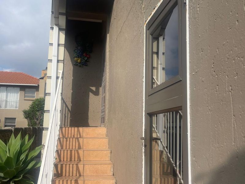 An exterior view of a rear staircase with tiled steps and metal balustrade leading to an upper level entrance.
