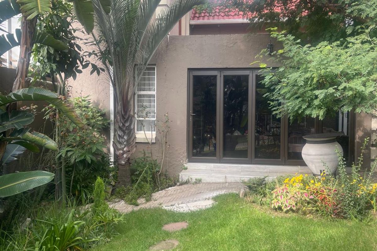 A private rear garden featuring a lush lawn, mature trees, and a paved pathway leading to modern sliding glass doors.