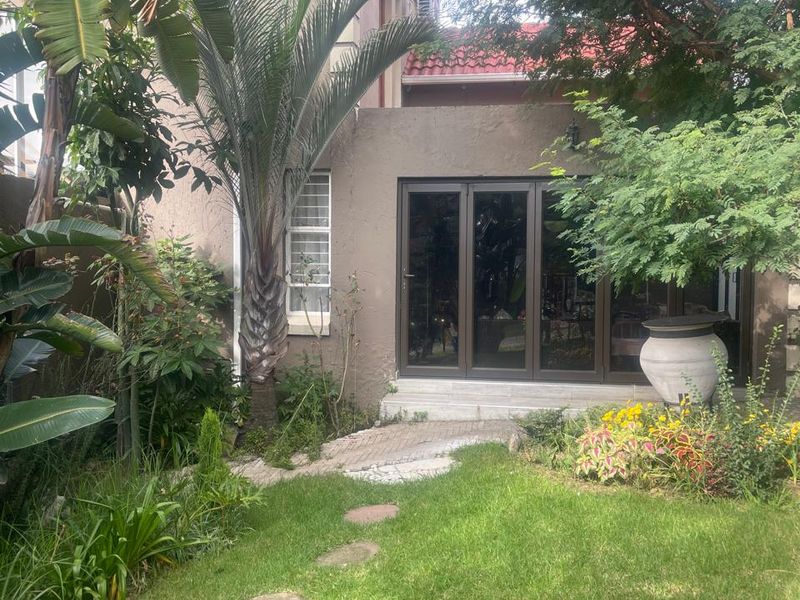 A private rear garden featuring a lush lawn, mature trees, and a paved pathway leading to modern sliding glass doors.