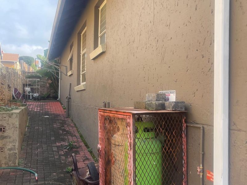 Side exterior area featuring a paved walkway, external wall, and a metal gas cylinder storage cage.