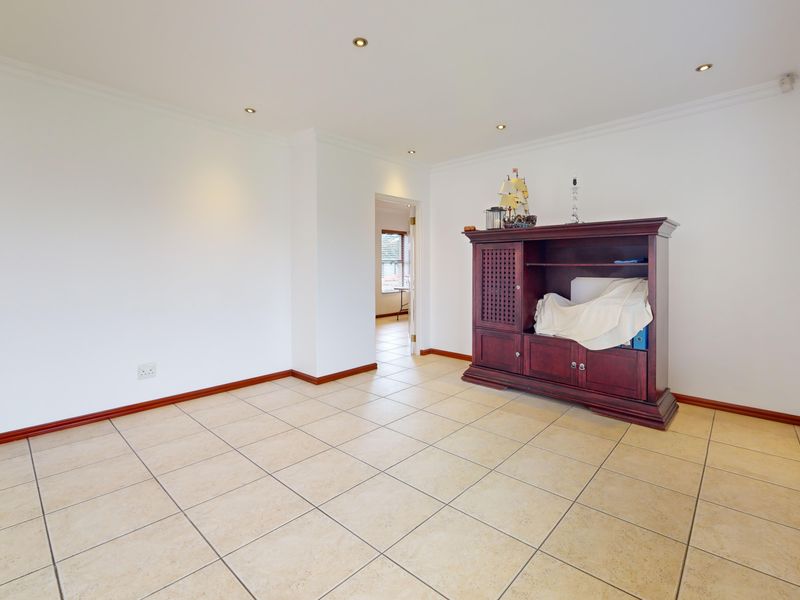 A bright and spacious living area featuring neutral ceramic floor tiles, recessed downlighting, and clean white walls, offering a versatile space for living.