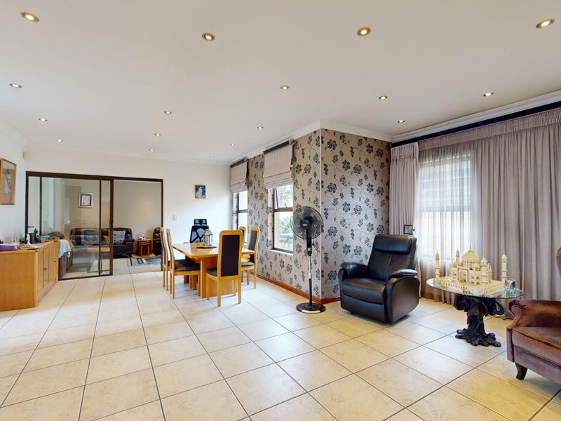 Spacious open-plan living and dining area featuring tiled flooring, recessed lighting, and a decorative wallpaper feature wall with access to an adjacent room.