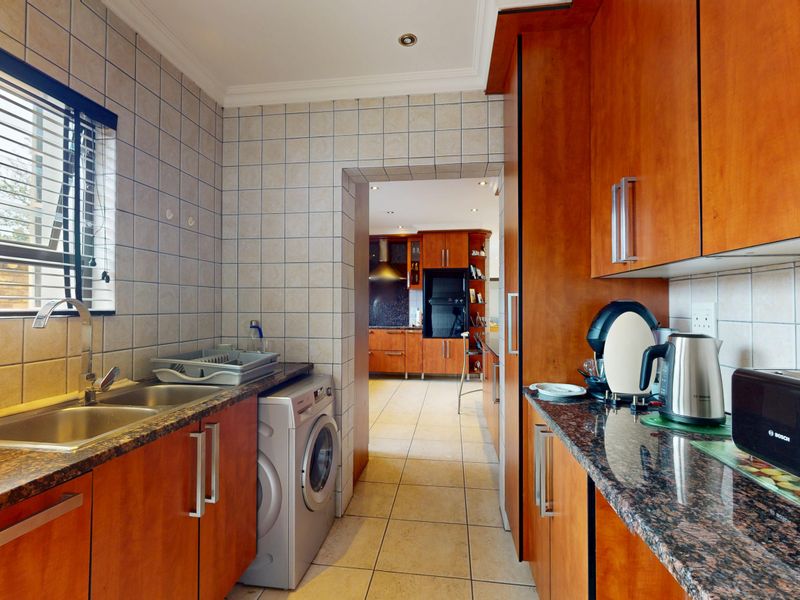Functional scullery featuring granite countertops, double sink, tiled splashbacks, and built-in wooden cabinetry with direct access to the main kitchen area.