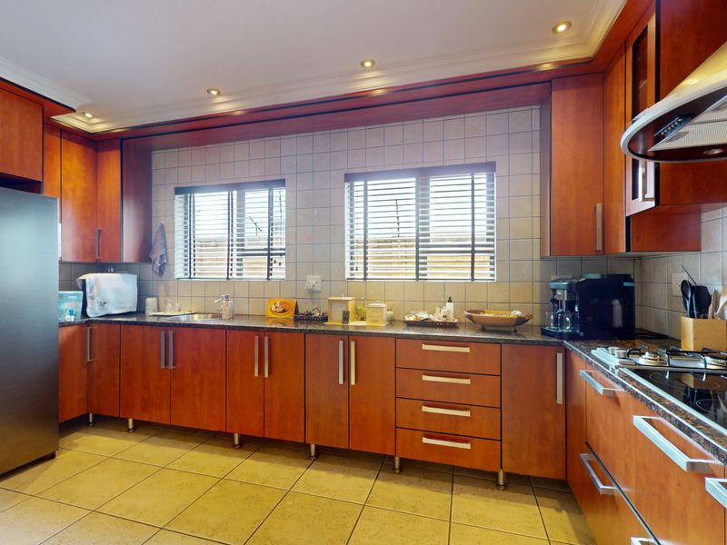 A functional kitchen featuring cherry wood cabinetry, granite countertops, a built-in gas hob, and a stainless steel extractor fan with tiled splashbacks.