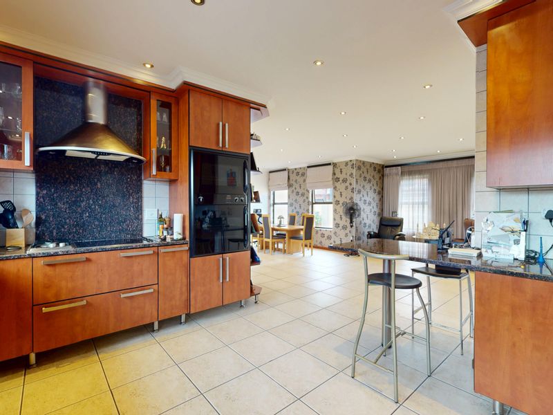 Spacious open-plan kitchen and dining area featuring wood-finish cabinetry, granite countertops, integrated appliances, and neutral ceramic floor tiles.