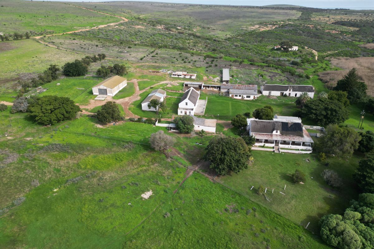Aerial view of a rural farm property featuring a main farmhouse, multiple outbuildings, and expansive surrounding agricultural land.