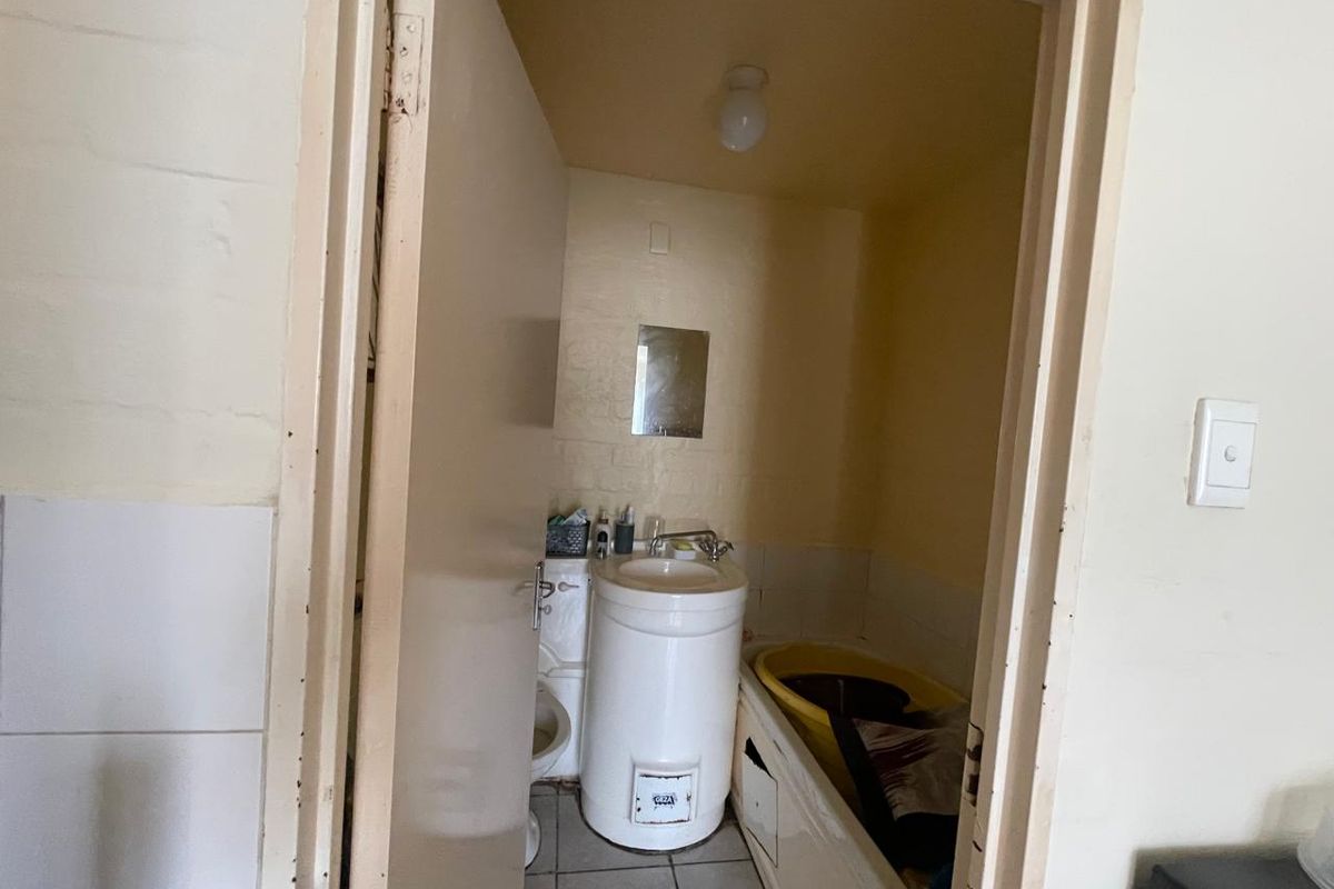 A compact bathroom featuring a pedestal basin, toilet, and bathtub with tiled flooring, requiring cosmetic updates to improve its overall condition.