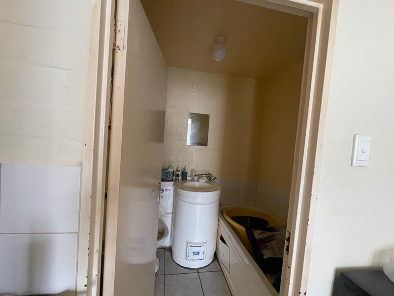 A compact bathroom featuring a pedestal basin, toilet, and bathtub with tiled flooring, requiring cosmetic updates to improve its overall condition.