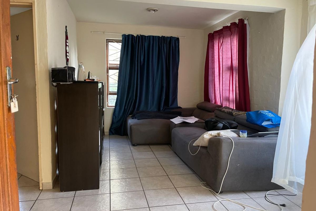 A living room area featuring ceramic floor tiles and a window with security bars, offering a functional space ready for cosmetic updates.