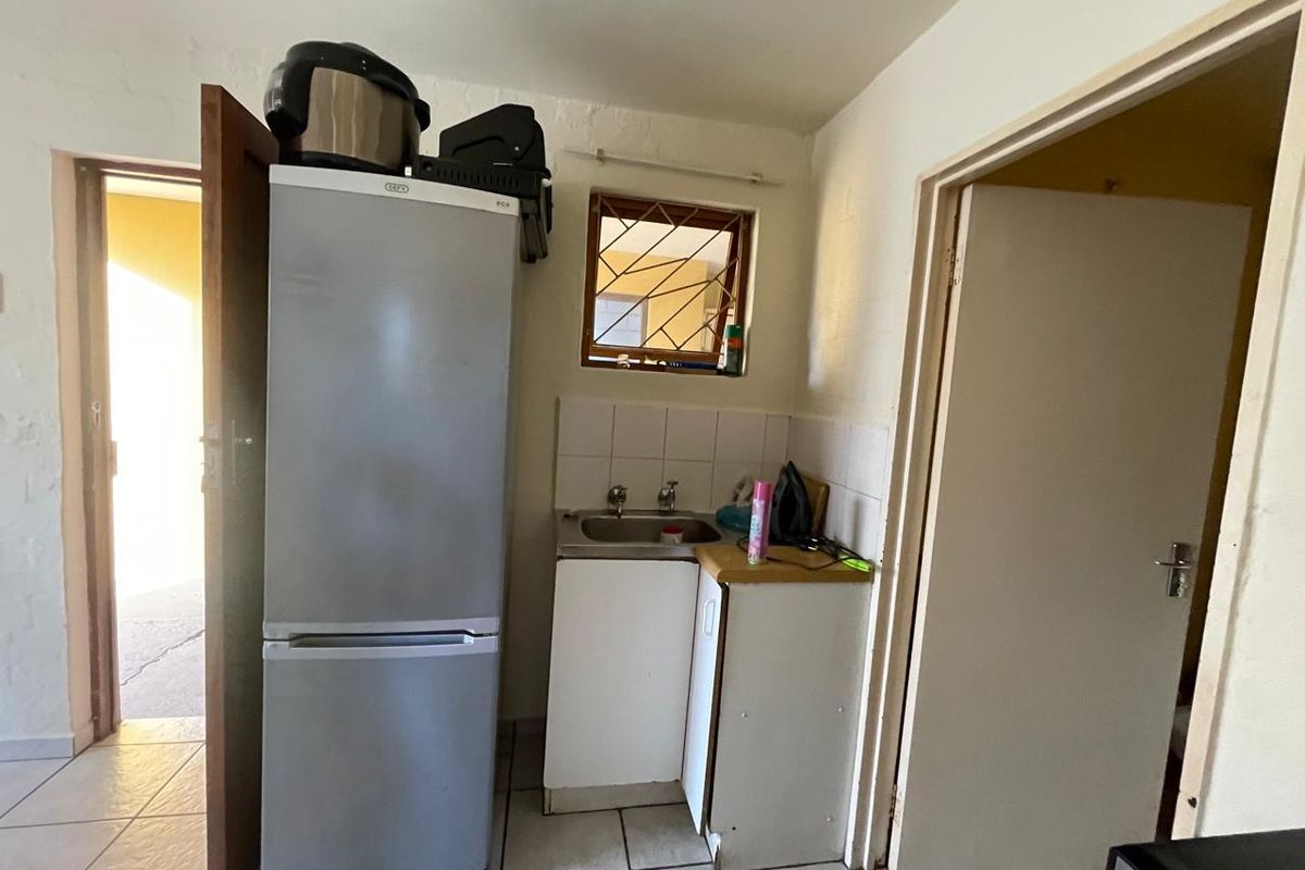 A compact scullery area featuring a stainless steel sink, tiled splashback, and tiled flooring, providing a functional utility space.