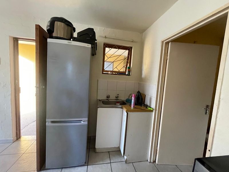A compact scullery area featuring a stainless steel sink, tiled splashback, and tiled flooring, providing a functional utility space.