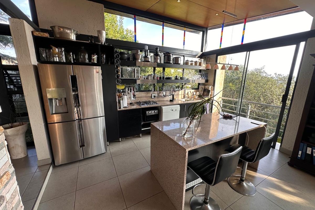 Modern kitchen featuring a granite island, built-in gas hob, oven, and extensive open shelving, complemented by large windows offering natural light and scenic views.