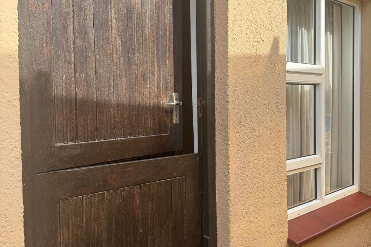 A rear exterior view featuring a dark wood stable door and a white uPVC window set against a textured stucco wall with tiled patio flooring.
