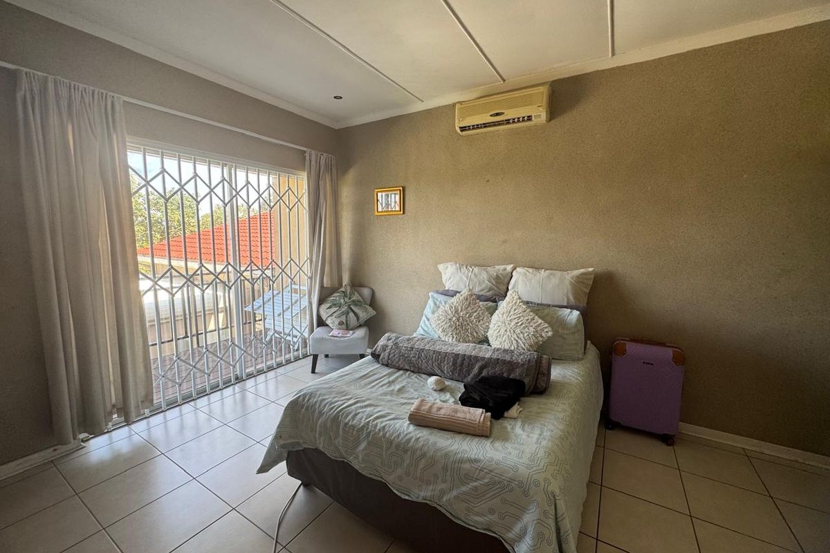 A bedroom featuring tiled flooring, a split-system air conditioner, and a sliding glass door with a security gate leading to an outdoor area.