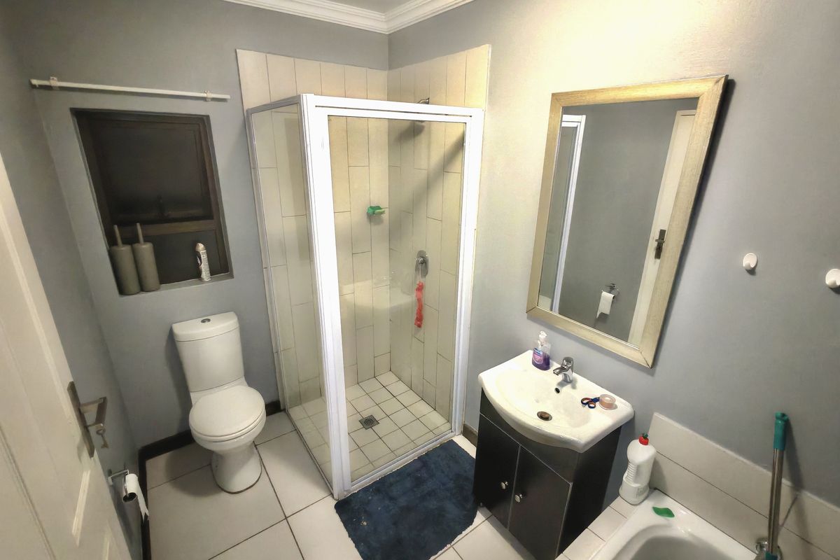 A functional bathroom featuring a corner shower enclosure, a vanity with basin, a toilet, and tiled flooring.