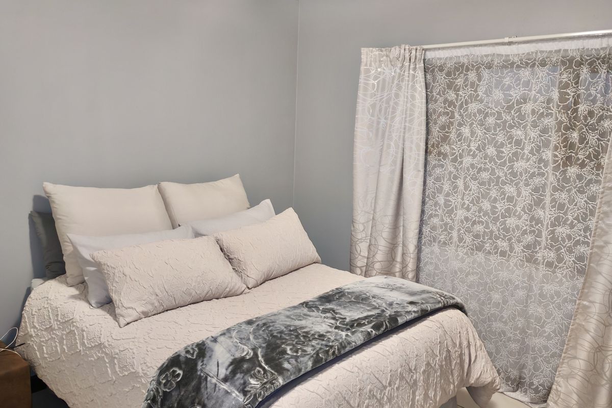 A bedroom featuring neutral wall paint, tiled flooring, and a window dressed with layered curtains.