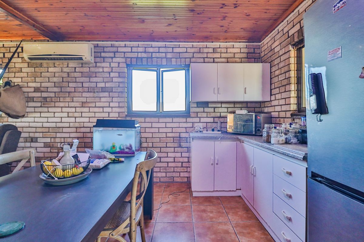 A rustic kitchen featuring exposed brick walls, timber ceiling, tiled flooring, and built-in cabinetry with granite-style countertops.