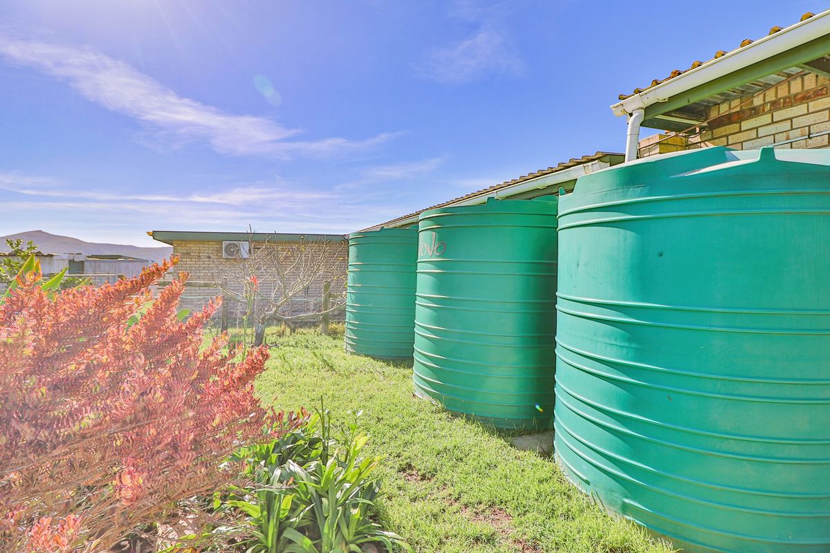 Exterior view of the property featuring multiple large green water storage tanks installed alongside the building structure.
