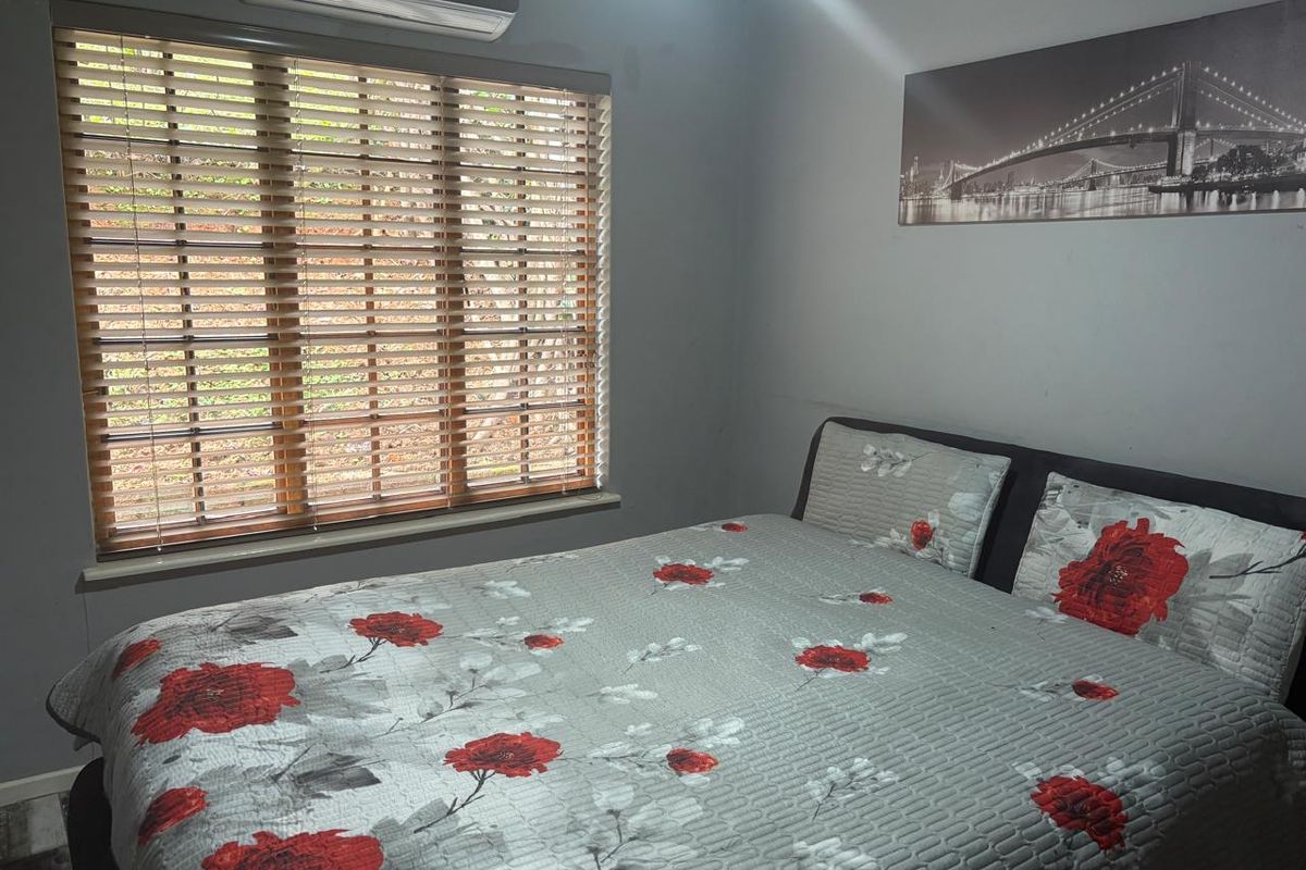 A functional bedroom featuring a wall-mounted split-system air conditioner and wooden venetian blinds.
