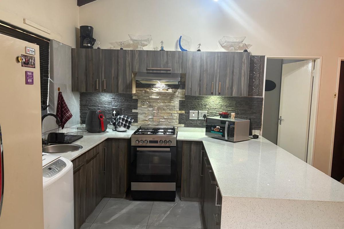 Modern kitchen featuring dark wood-grain cabinetry, stone countertops, a gas stove with extractor fan, and a stone tile backsplash.
