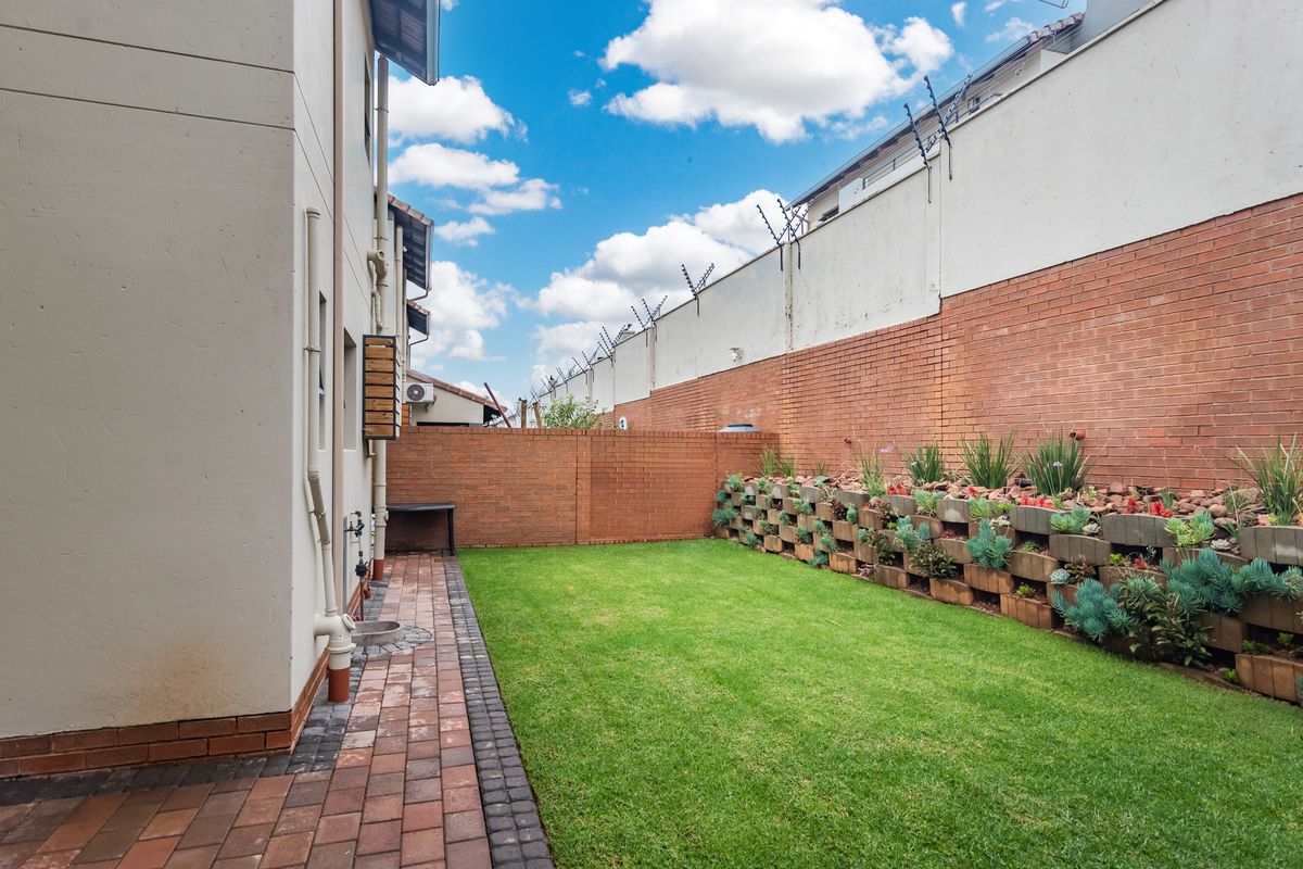 A private rear garden featuring a paved walkway, a well-maintained lawn, and a tiered brick retaining wall with established plantings.