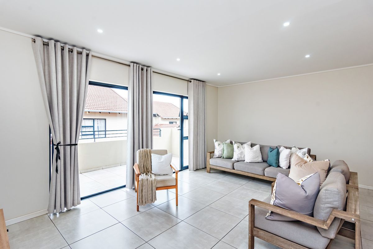 Bright and spacious living room featuring large format floor tiles, recessed downlighting, and dual sliding glass doors providing access to an outdoor balcony.