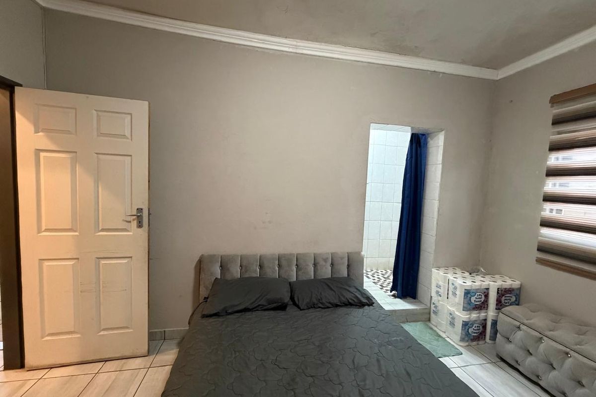 A bedroom featuring tiled flooring, coved ceilings, and an en-suite bathroom access point. The room requires cosmetic updates to address wall and ceiling wear.