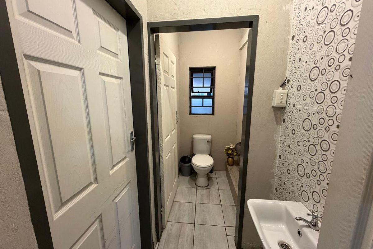 A small bathroom featuring a toilet, wall-mounted basin, and tiled flooring, requiring some finishing work on the walls and electrical fixtures.